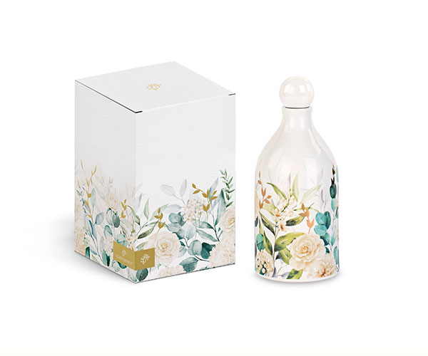 ottiglia di Olio BLOOM LOVE da 300 ml e scatola abbinata su uno schermo di computer. La bottiglia e la scatola sono decorate con un motivo floreale botanico sui toni del bianco, verde e pesca/rosa chiaro. L'articolo è identificato come