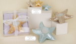 Composizione di bomboniere a tema marino con stelle marine in porcellana azzurre, oro e bianche in versione magnete da 6cm e porta candela da 14cm.