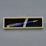 Elegante penna bomboniera per laurea di colore blu con finiture dorate e corpo superiore trasparente con perline blu, adagiata nel suo astuccio regalo bianco con interno nero.