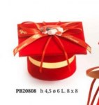 Tocco laurea porta confetti 20808 Cofanetto portaconfetti rotondo in velluto rosso con base cilindrica e coperchio quadrato decorato con nastro rosso e un piccolo fiorellino. Il nastro porta la scritta